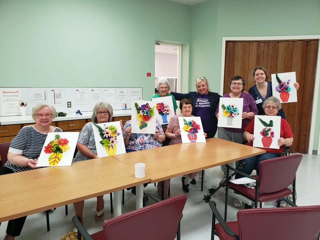 Seniors at a Euro-American Homecare art class holding their flower paintings