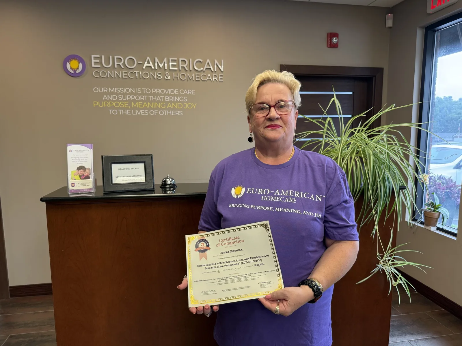 Caregiver Joanna holding her dementia-care training certificate in the Euro-American Homecare office