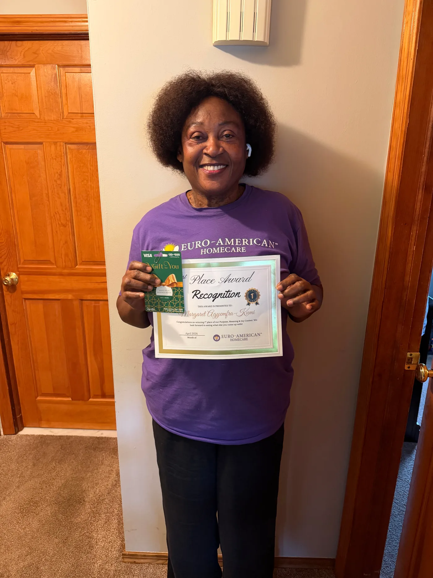 A caregiver at home holding her award certificate and gift card