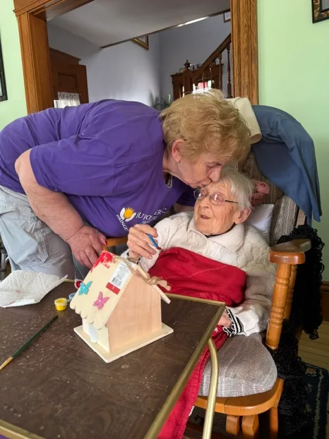 A caregiver sharing an affectionate moment with her client while decorating a birdhouse