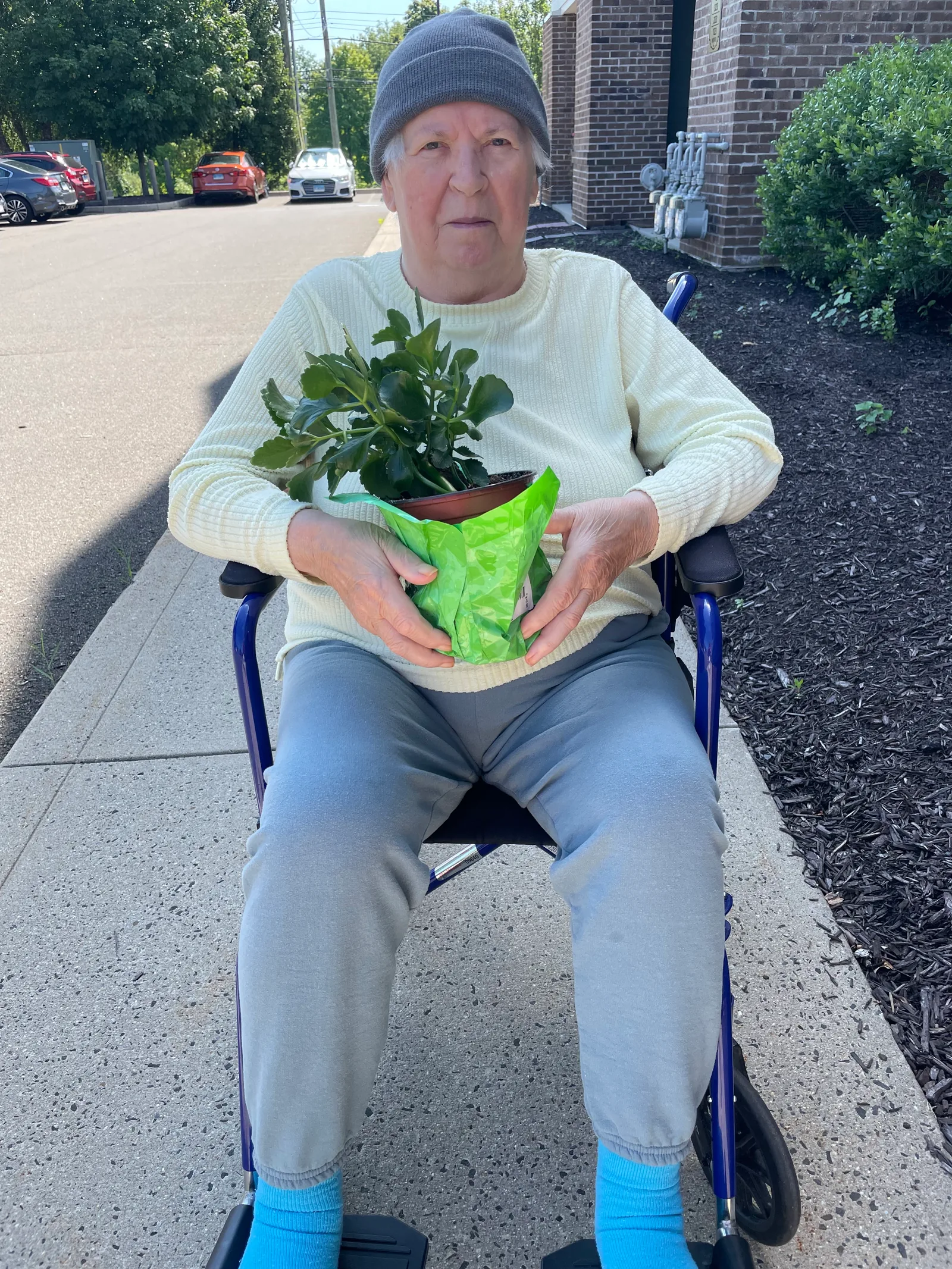 A client sitting outdoors in a wheelchair, proudly holding a potted houseplant