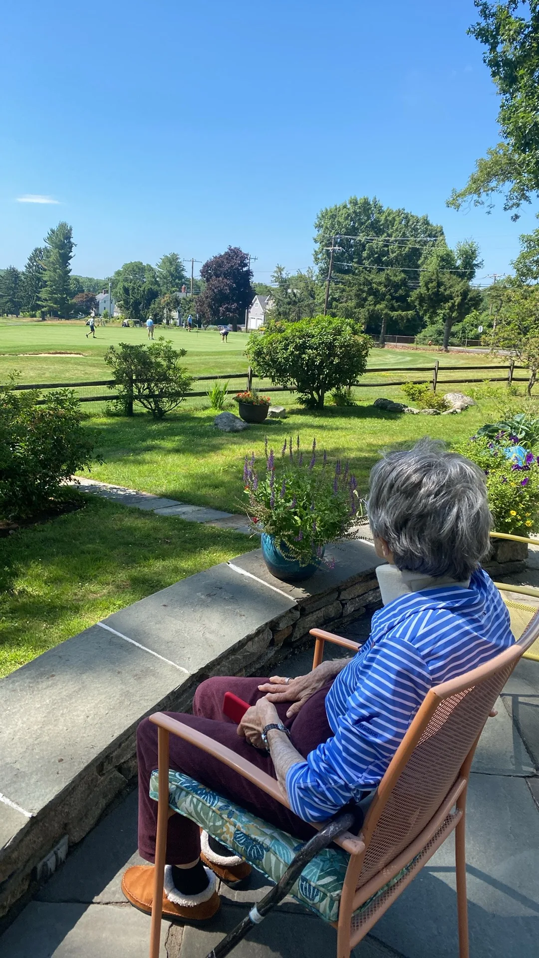 A client relaxing in a patio chair, watching golfers on the green beyond the yard